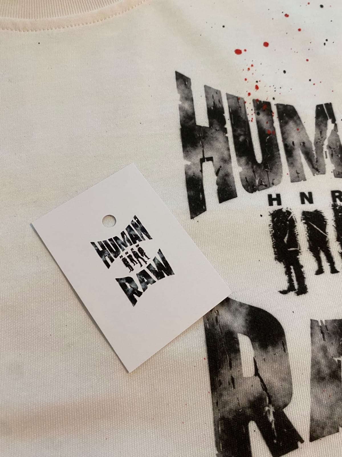 Cartellino Human Raw appoggiato sulla t-shirt